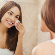 Staying fresh and clean. Beautiful young woman touching her face with sponge and smiling while standing in front of the mirror