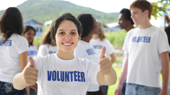happy volunteer girl showing thumbs up sign, group in background