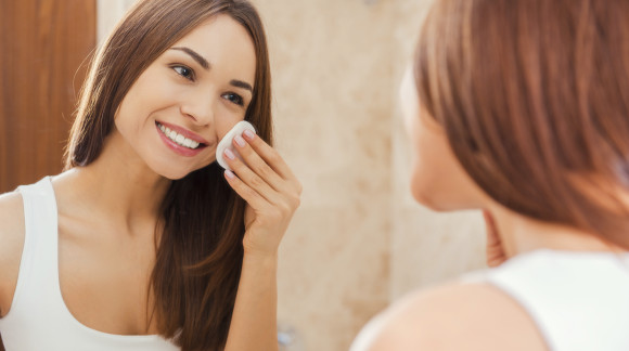 Staying fresh and clean. Beautiful young woman touching her face with sponge and smiling while standing in front of the mirror