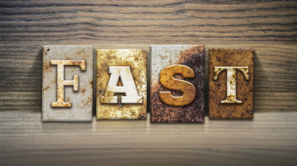The word "FAST" written in rusty metal letterpress type sitting on a wooden ledge background.