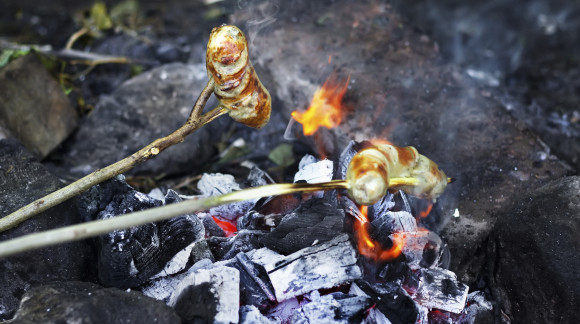 Sausages on sticks are frying on open fire outdoor