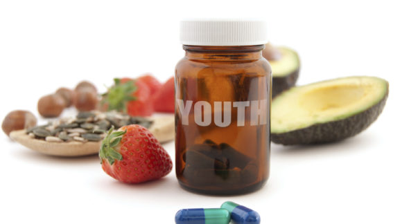 Anti-aging pills surrounded by nutritious superfoods including avocado, pumpkin seeds and berries